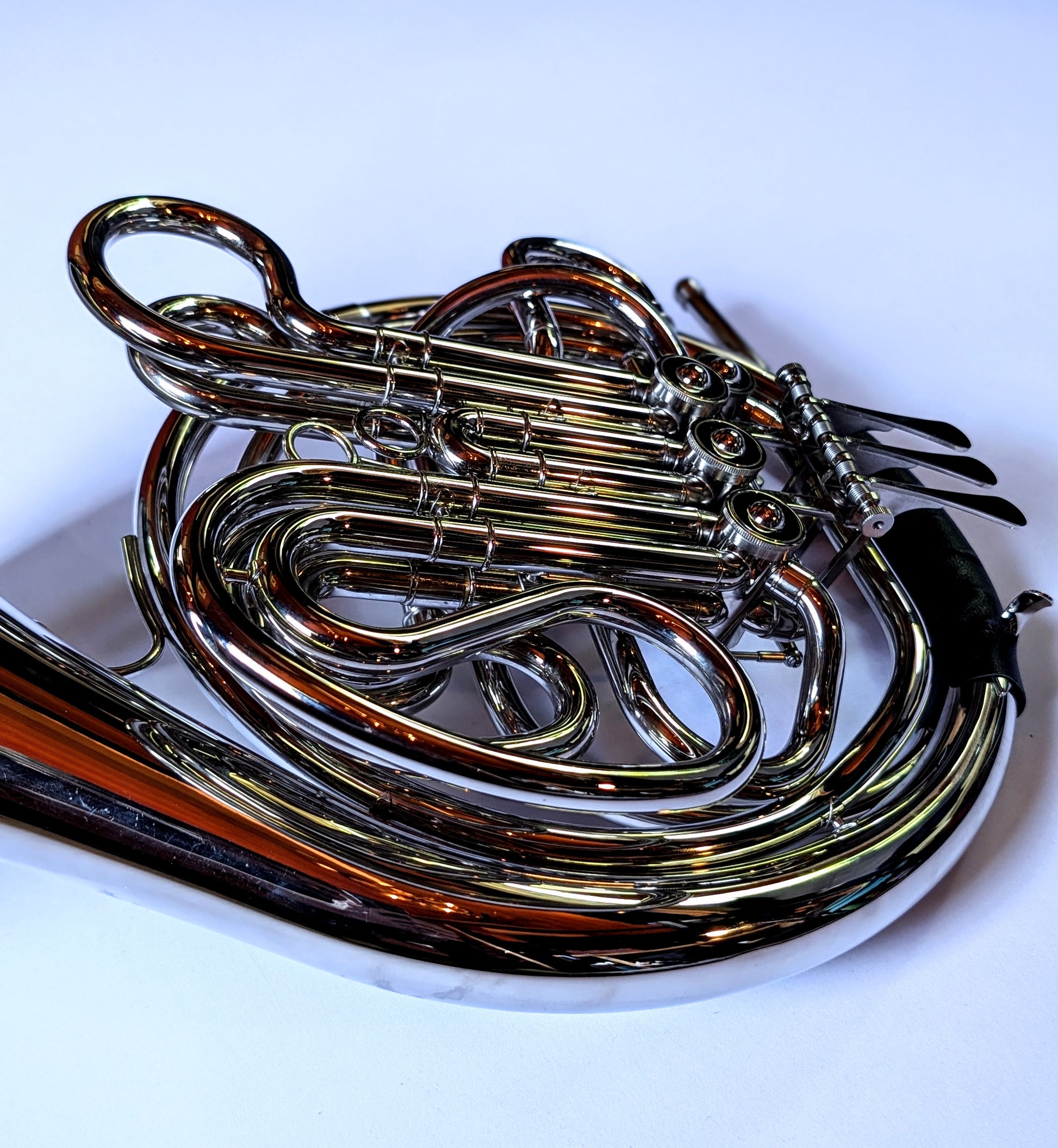 Silver-plated double French horn with F and Bb sides, thumb trigger mechanism, coiled tubing, and bell facing right